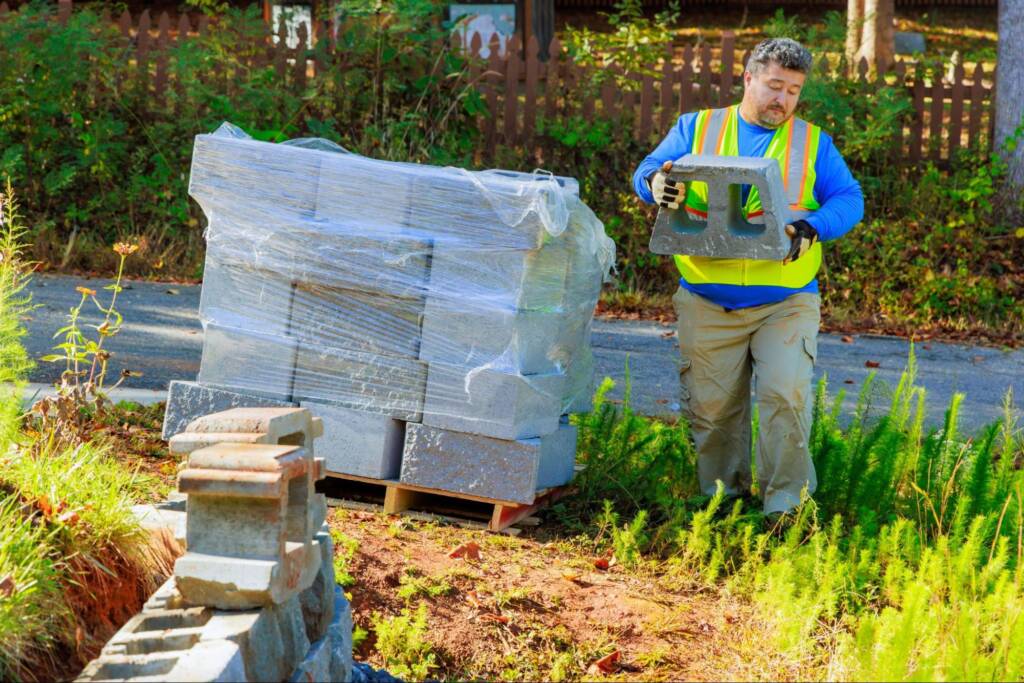 A landscape contractor installs concrete retaining wall blocks on-site for a new property.