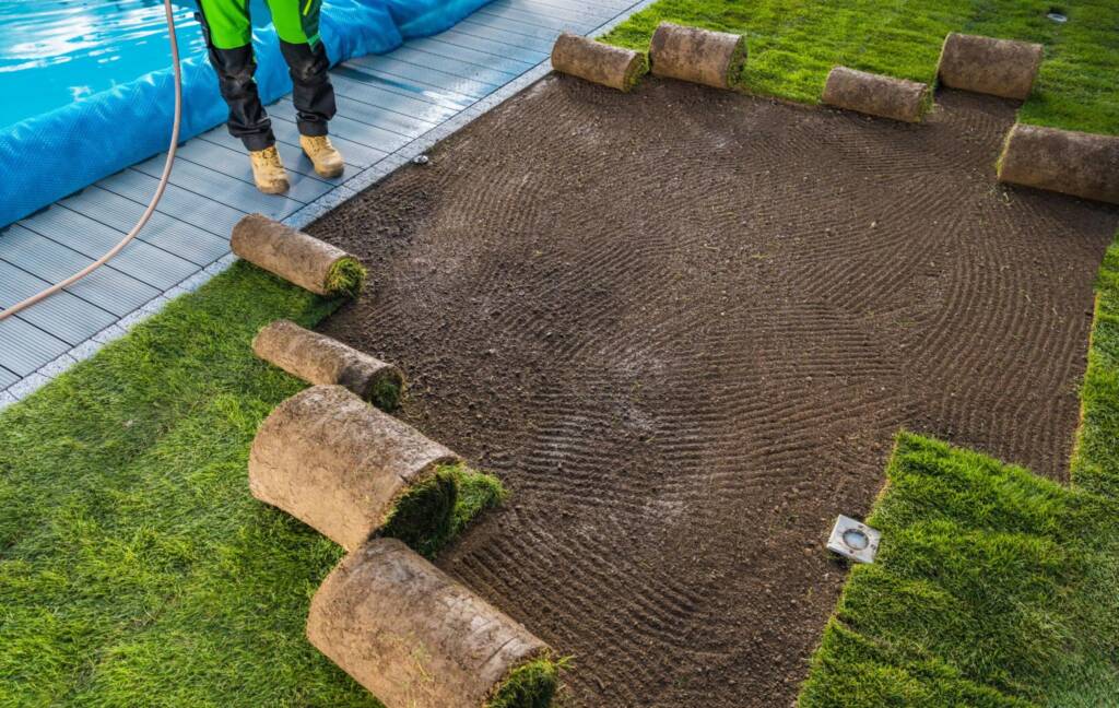 Cropped view of a landscaping worker installing turf rolls in a garden to create a new lawn.