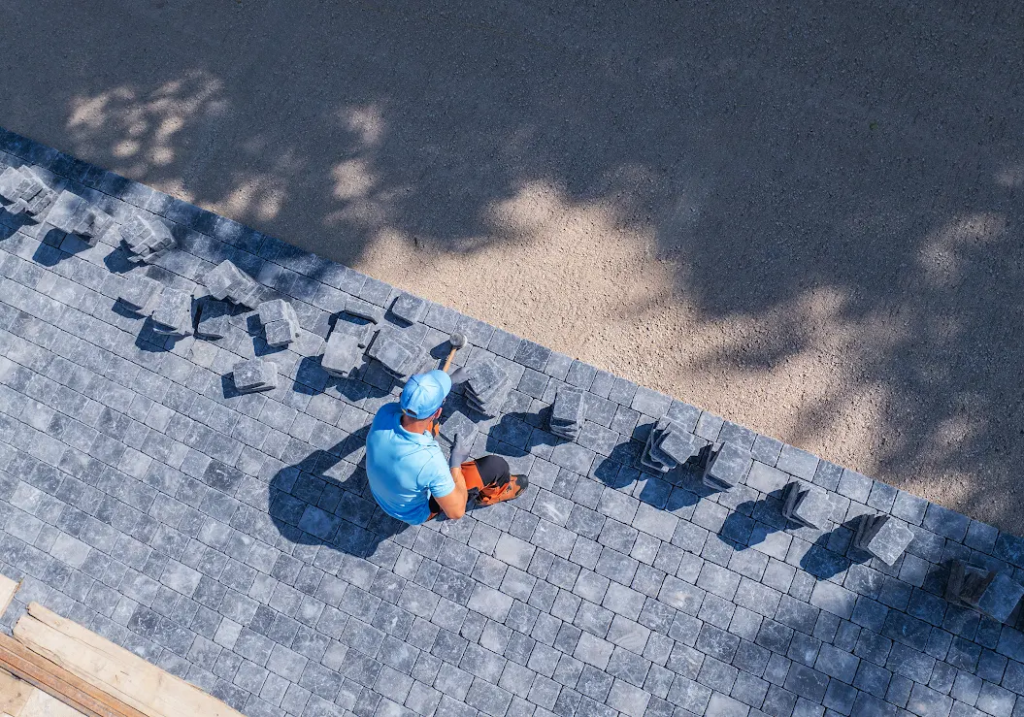 A worker in a blue uniform installs concrete pavers row by row.