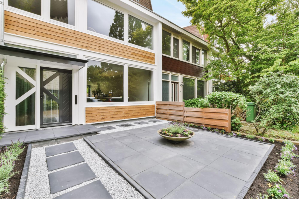 Entry with a black-framed glass door and a well-arranged landscape paver design near a garden