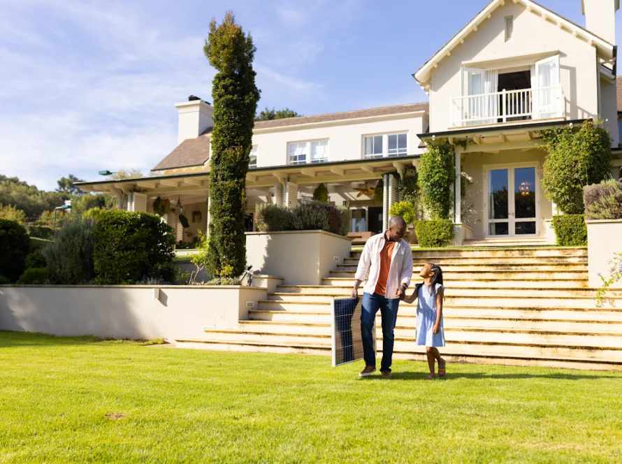 A father and daughter hold hands and walk over their front lawn.