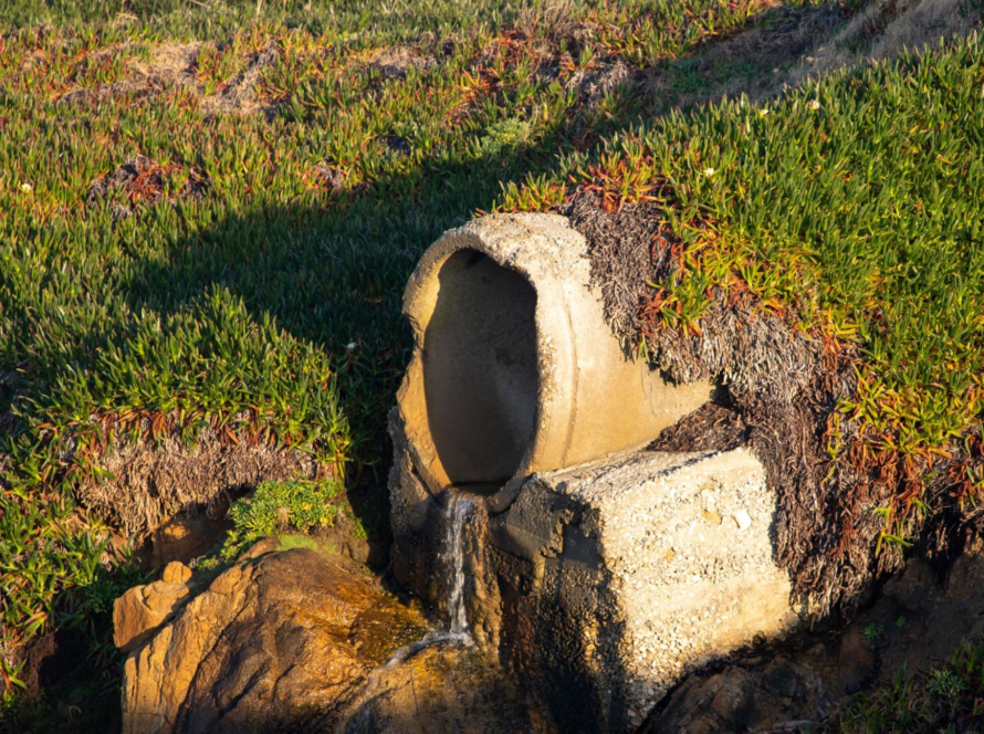 A culvert-style pipe directing surface runoff into a natural drainage area