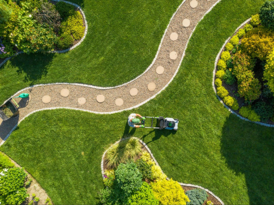 Aerial view showing a gardener mowing a lawn within a splendid landscaping layout