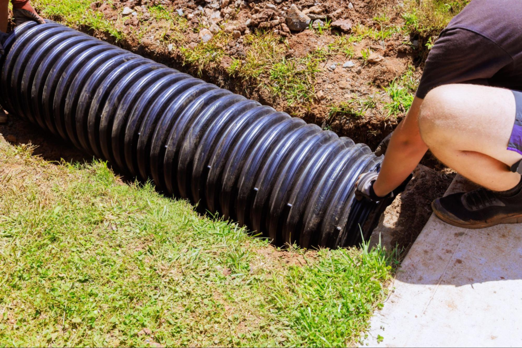 A worker placing black plastic pipes that channel rainwater into a central collection system